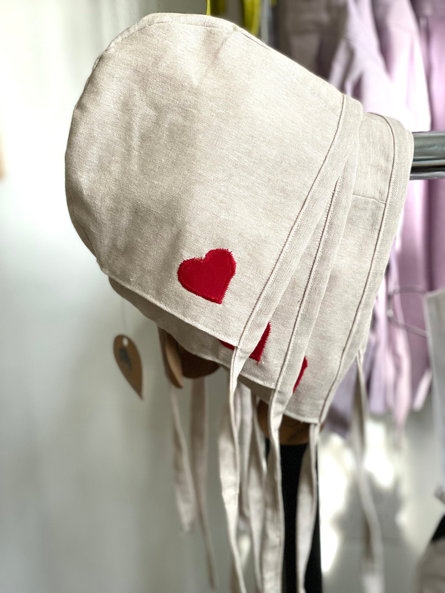 Stack of flax baby bonnets with embroidered heart detail.