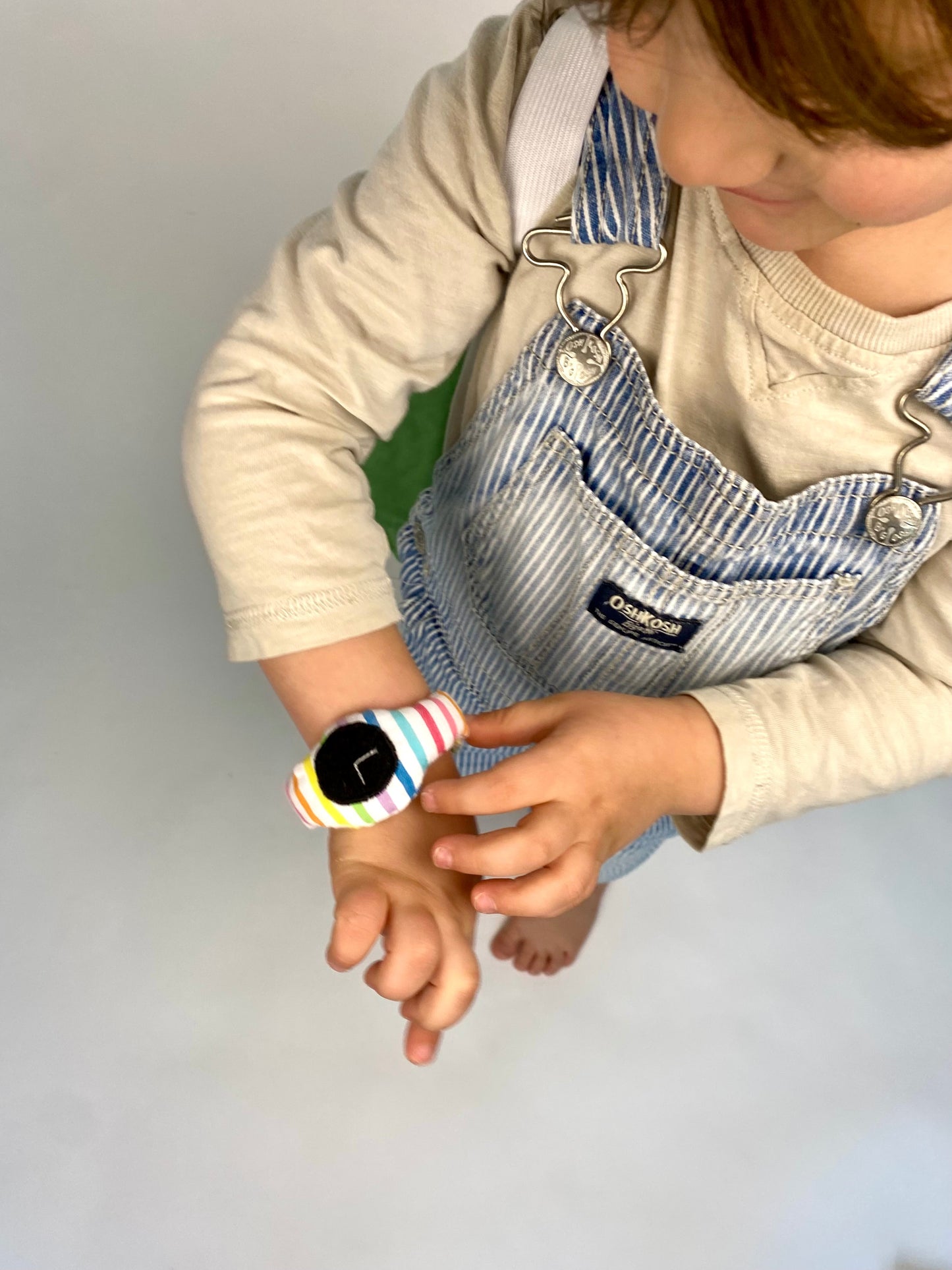 Toddler reads time on toy plush rainbow watch.
