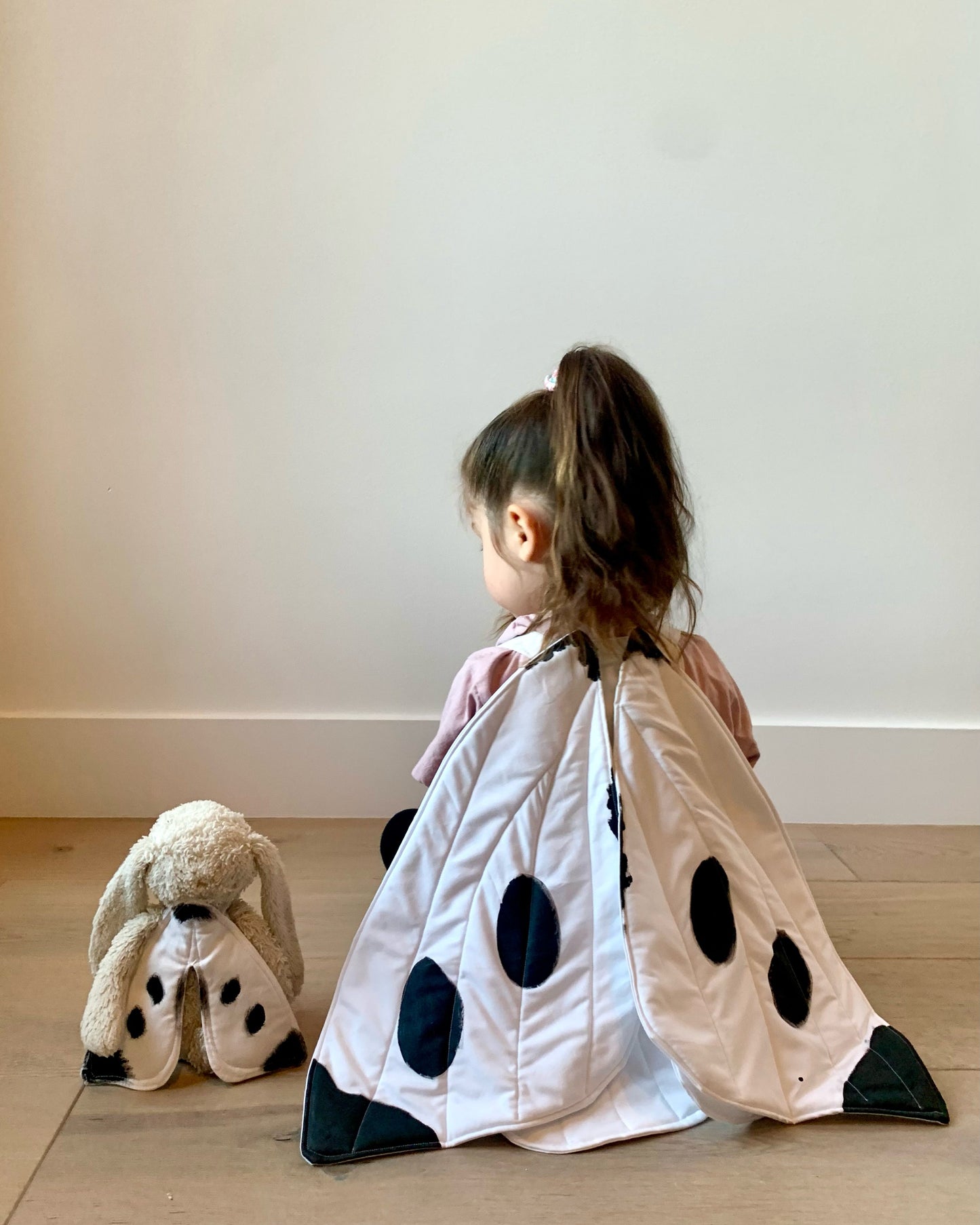 Girl sits next to matching doll wearing spotted butterfly wings